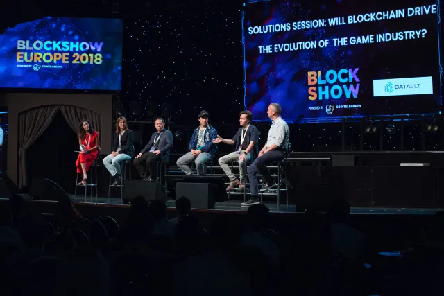 A panel of six speakers seated on stage at BlockShow Europe 2018 in front of a large conference screen.