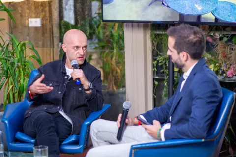 Two men in a fireside chat on blue armchairs at Crypto Party, one holding a Cointelegraph microphone, sponsor logos on the screen behind.