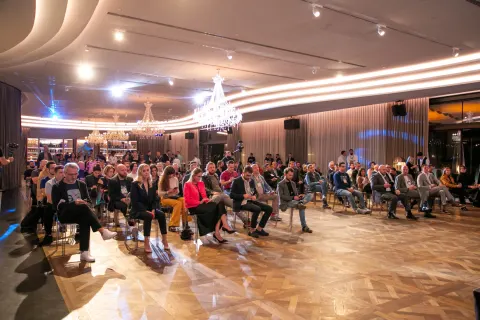 An audience seated in an elegant chandelier-lit ballroom for a talk.
