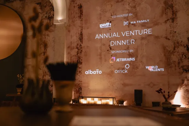 A wall projection reading 'Annual Venture Dinner' with co-host and sponsor logos, lit candles in the foreground.