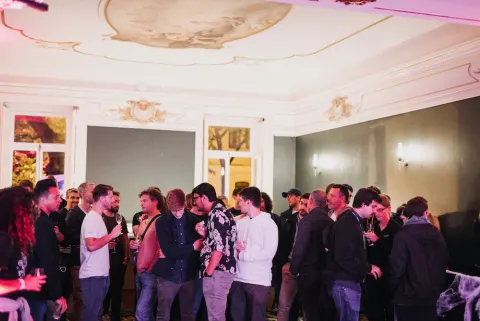 Four people talking and holding glasses of red wine at an event in a pink-lit room.
