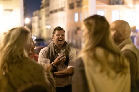 A group of people chatting at night on a Lisbon street lined with colorful building facades.