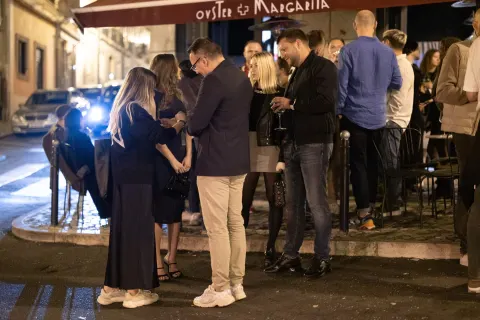 A group of people chatting at night on a Lisbon street lined with colorful building facades.