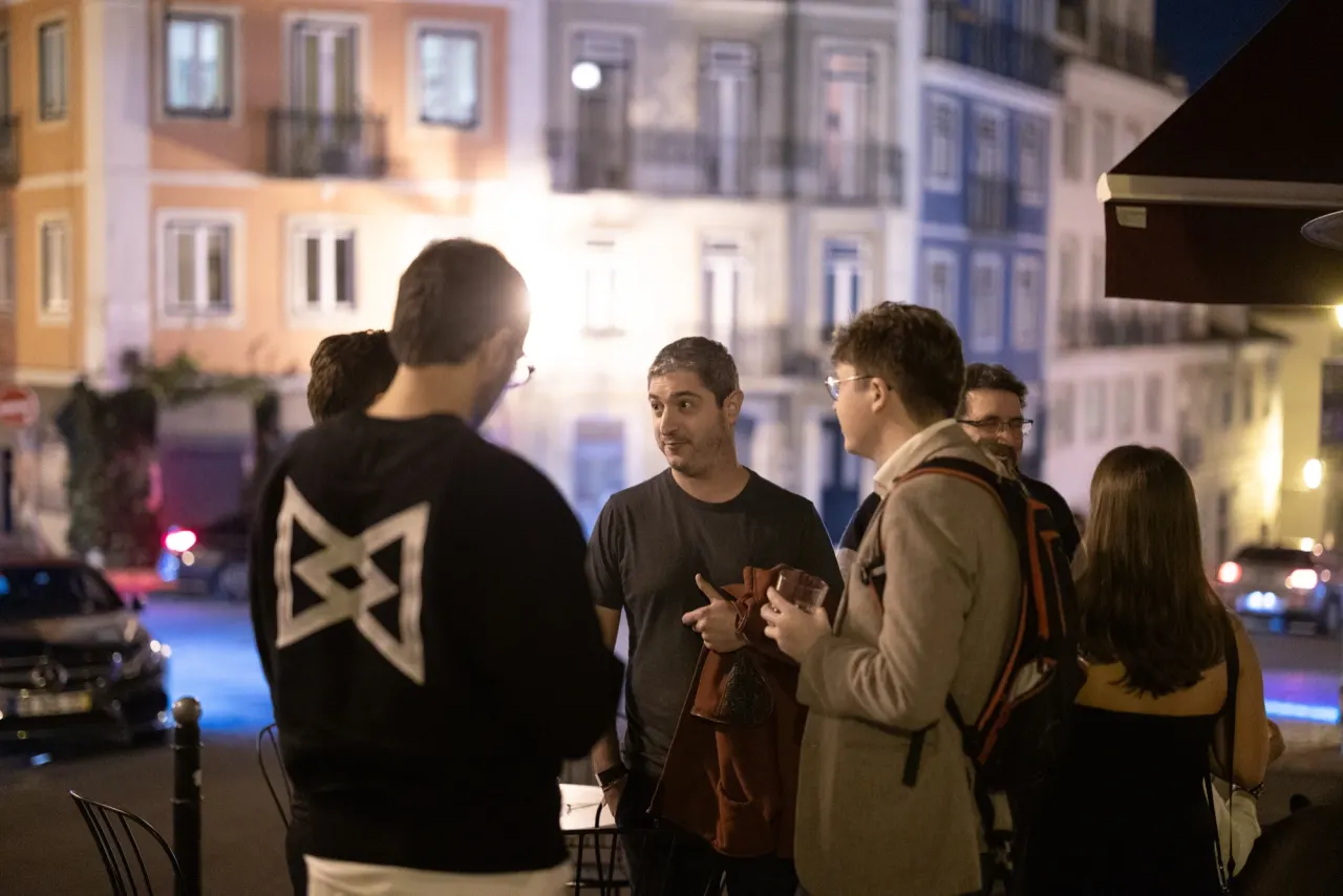 A group of people chatting at night on a Lisbon street lined with colorful building facades.
