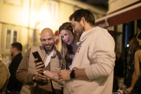 A group of people chatting at night on a Lisbon street lined with colorful building facades.