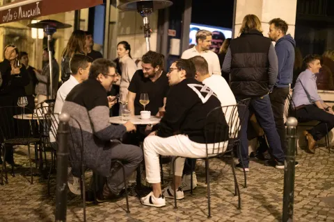 A group of people chatting at night on a Lisbon street lined with colorful building facades.