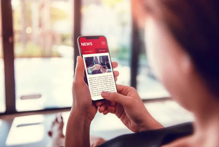Over-the-shoulder view of a person reading a red NEWS app on a smartphone.