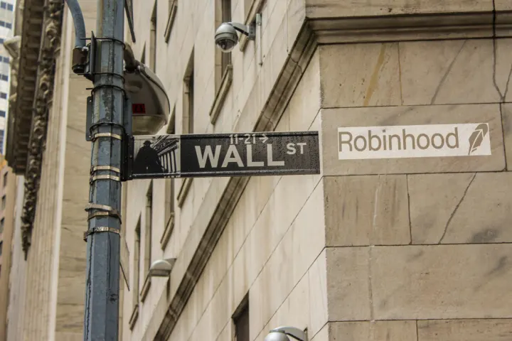 A 'Wall St' street sign beside a Robinhood logo sign on the corner of a stone building.