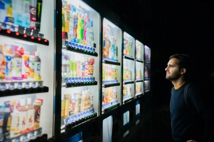 A man looking at a row of brightly lit vending machines at night.