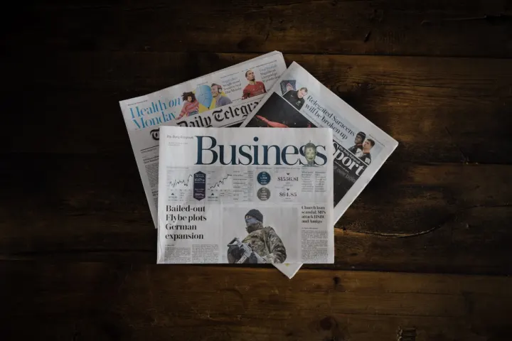 Folded Daily Telegraph newspapers, business section on top, fanned out on a dark wooden table.
